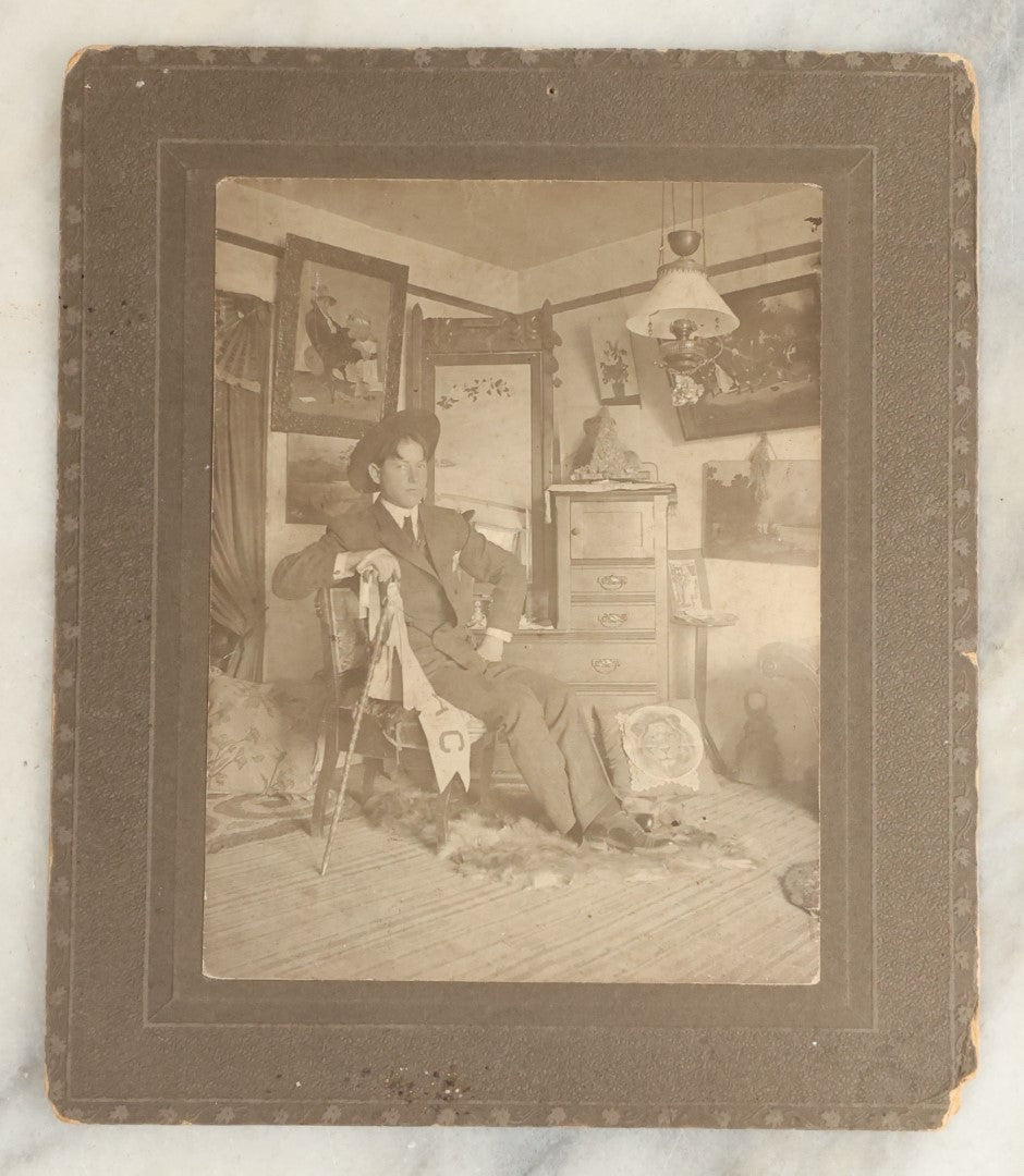 Lot 120 - Antique Boarded Photo Of A Young Man College Student, Likely In A Dorm Room, With Interior Scene Including Artwork, Early Light Fixture, Dresser, Pennant, Fur Rug, And More