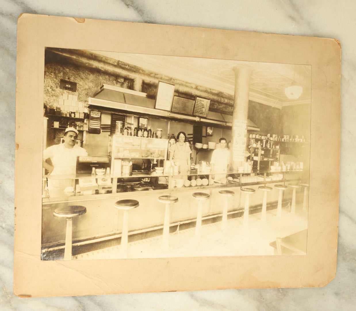 Lot 081 - Antique Boarded Photograph Of A Classic American Diner, With Workers Behind The Counter, Lots Of Signage, Stools
