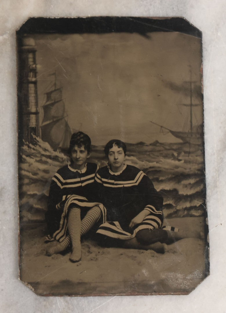 Lot 074 - Single Antique Tintype Photograph Of Two Victorian Ladies In Beachwear Posing On Real Sand Set With Painted Backdrop With Lighthouse And Ships