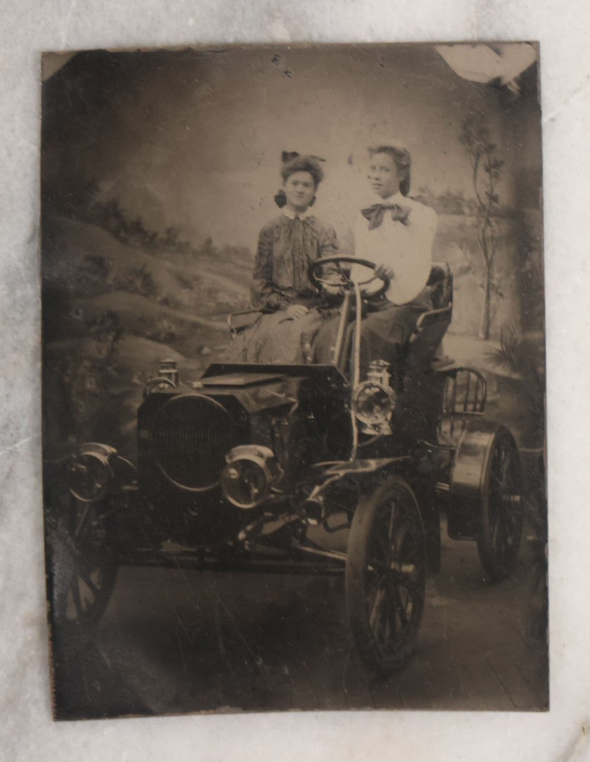 Lot 075 - Single Antique Tintype Photograph Of Two Ladies Posing In An Early Automobile In Studio With Landscape Backdrop