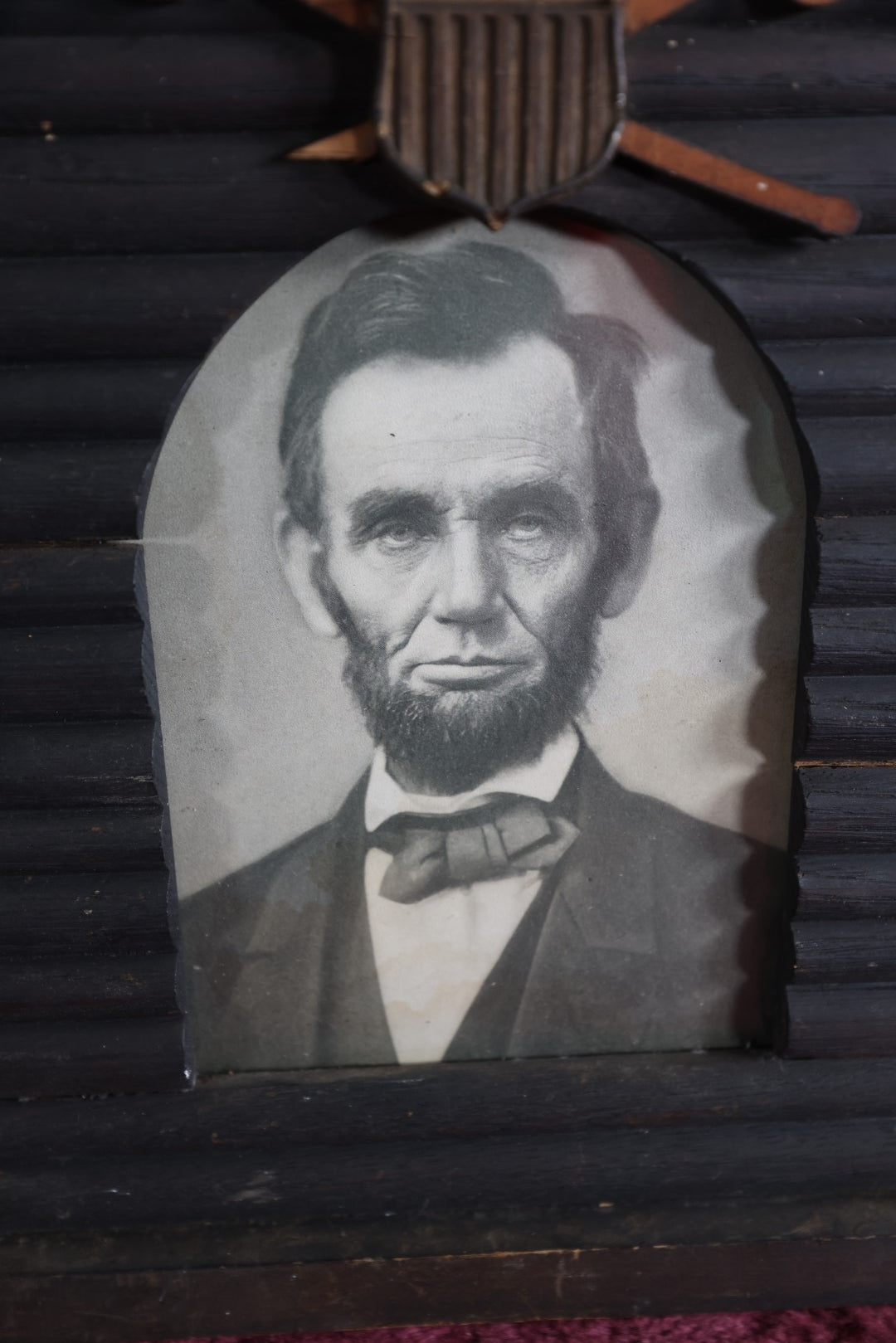 Lot 079 - Antique Print Of President Abraham Lincoln In Hand Made Log Cabin Frame With Patriotic Shield, Swords, Likely Grand Army Of The Republic Related, Note Losses To Wood