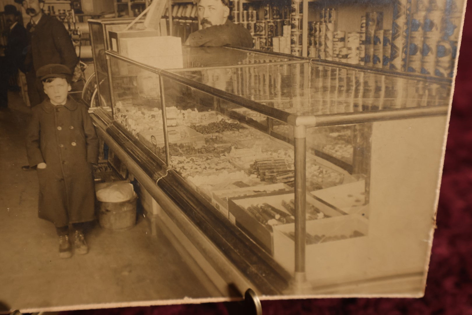 Lot 137 - Small Boarded Photo - General Store Interior Occupational Photo, Many Cans, Ads, Young Boy At Center, Men Around Wood Stove