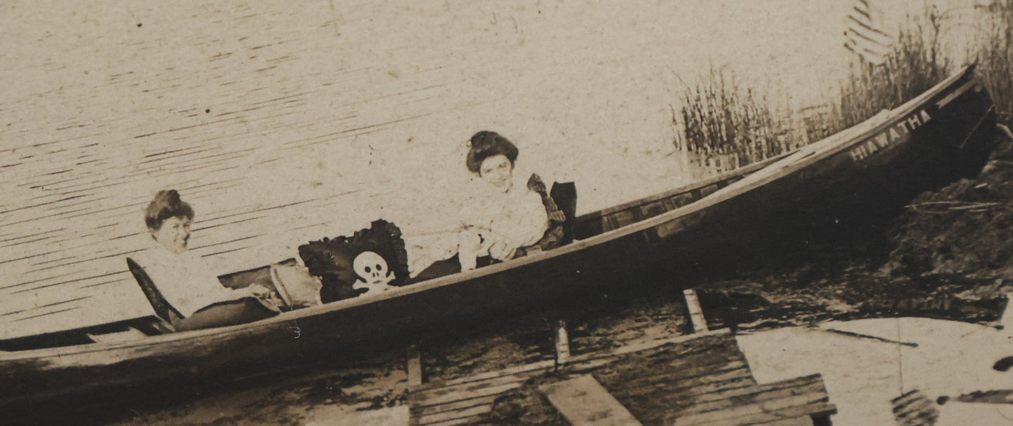 Lot 050 - Unusual Antique Framed Photo Of Two Women In A Canoe With A Skull And Crossbones / Jolly Roger Pillow, Boat Named Hiawatha, American Flag In Frame