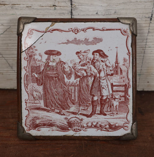 Lot 077 - Antique Painted Tile In Frame Trivet / Wall Hanger, Street Scene With Man, Baby, Pig, Dog, Church And Cemetery In Background, Note Severe Damage, Repairs