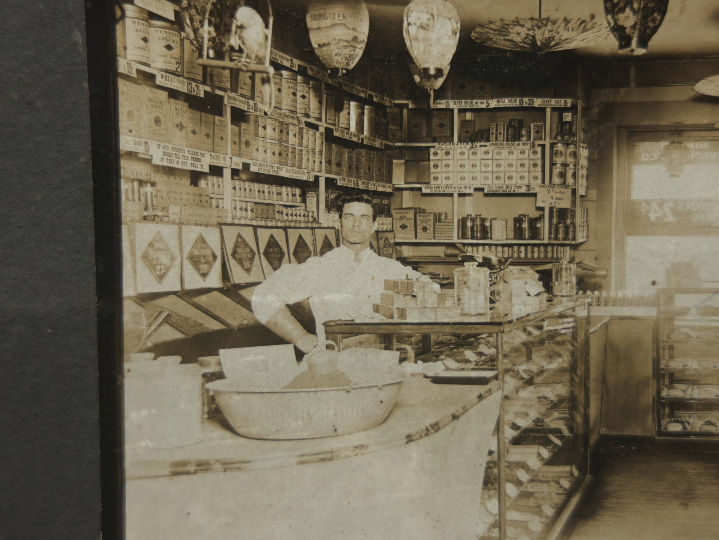 Lot 076 - Antique Boarded Occupational Photograph Of A Handsome Shopkeeper In A General Store, With Advertising, Chinese Lanterns With Tea Ads, And More, Note Bend In Corner