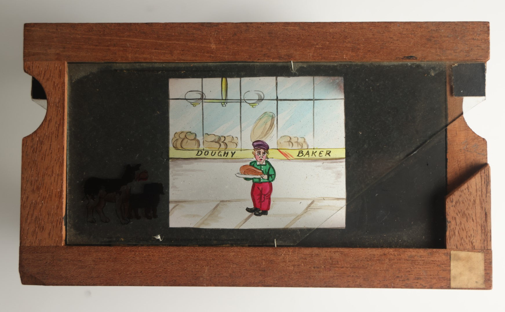 Lot 041 - Antique Hand Painted Animated Magic Lantern Motion Slide, Young Boy With Chicken Outside Bakery Surrounded By Dogs, Dogs Slide In From Both Sides