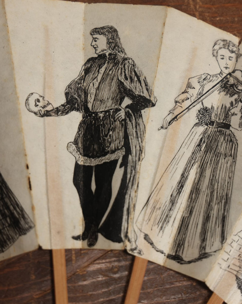 Lot 009 - Antique Varnished Paper Hand Fan With Original Pen And Ink Illustrations Of Many Characters, Actor With Skull, Woman With Dogs, Horse Riders, And More, Two Artist Signatures, Dated 1900