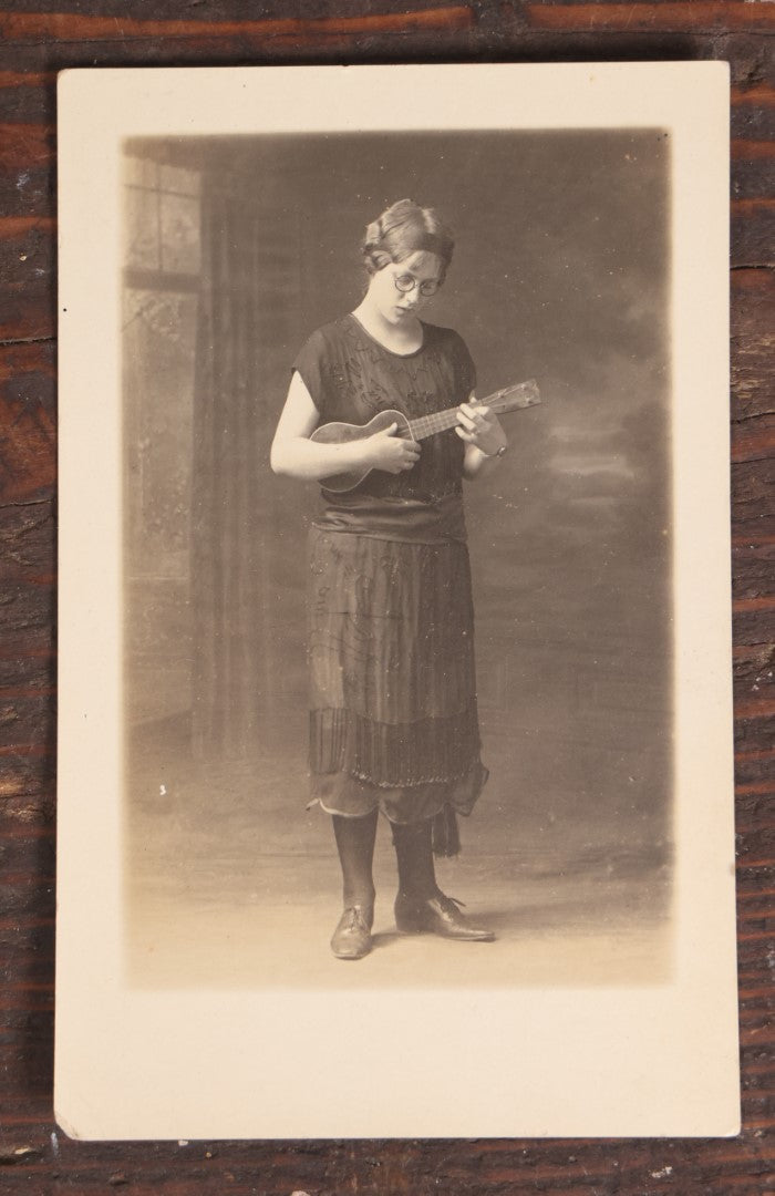 Lot 062 - Antique Real Photo Postcard R.P.P.C. Of A Young Woman In Glasses Playing A Ukulele, Possible Name Written On Back, Cora