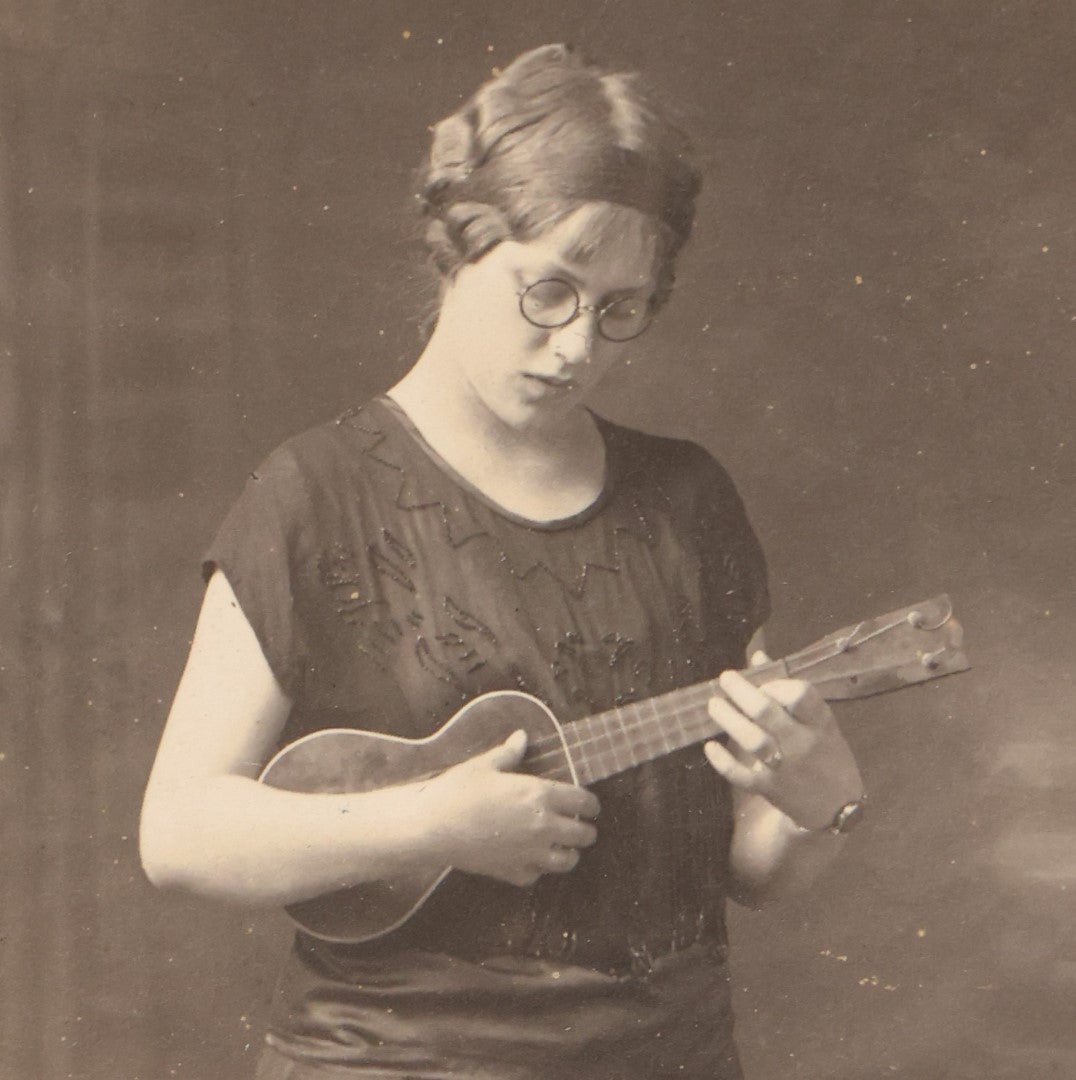 Lot 062 - Antique Real Photo Postcard R.P.P.C. Of A Young Woman In Glasses Playing A Ukulele, Possible Name Written On Back, Cora