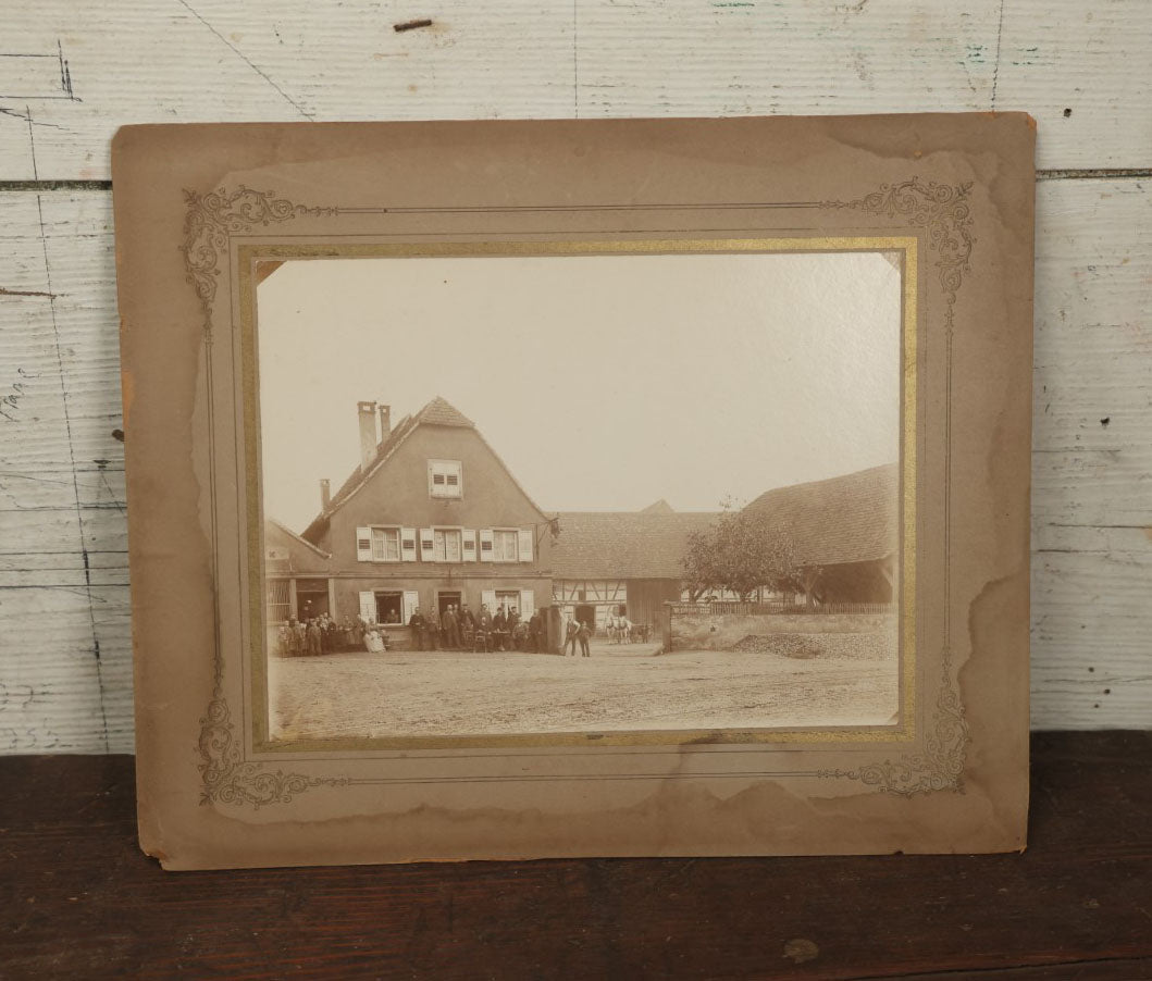 Lot 135 - Antique Boarded Photo Of A Large Group Of Photo Outside Of A Building With A Trade Sign Hanging From It, Horse Drawn Carriage In The Background, Men, Women, And Children, Unknown Location