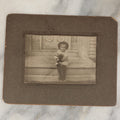 Lot 018 - Antique Boarded Photograph Of A Young Boy In A Hat Sitting On The Front Porch Stoop With A Small Black Cat In His Arms, Cat Moving, Blurry