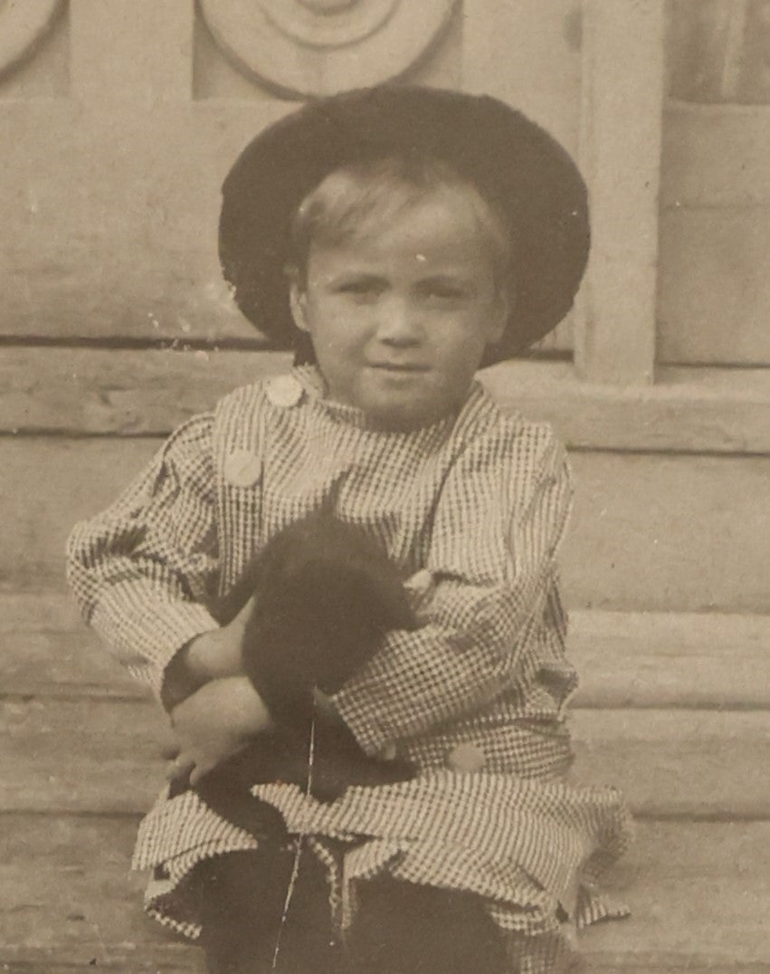 Lot 018 - Antique Boarded Photograph Of A Young Boy In A Hat Sitting On The Front Porch Stoop With A Small Black Cat In His Arms, Cat Moving, Blurry