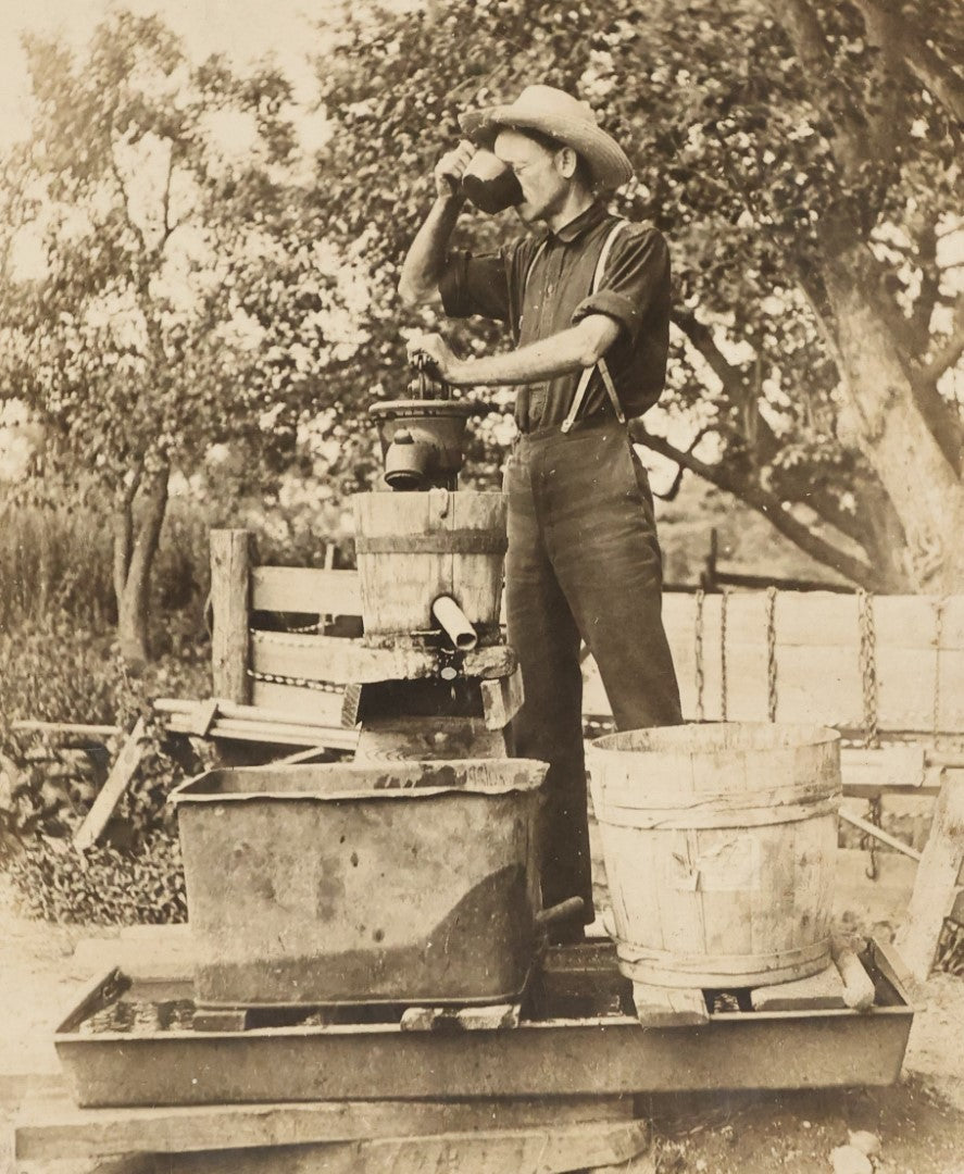 Lot 022 - Antique Boarded Occupational Photograph Of A Man Preparing A Beverage With A Press, Possible Moonshine Or Wine Making