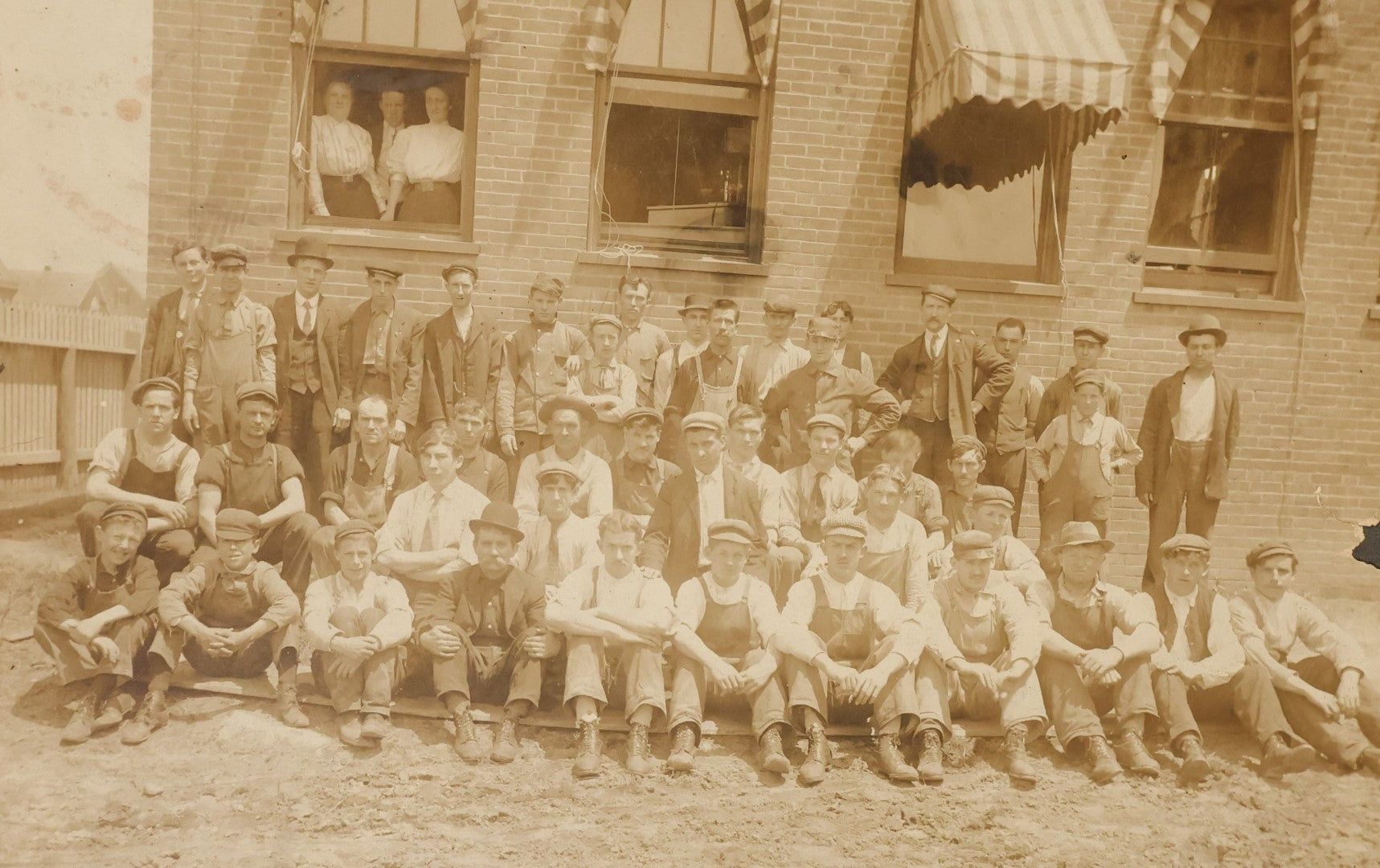 Lot 024 - Antique Boarded Occupational Photograph Of A Group Of Laborers Outside Of A Commercial Building, Note Ladies In Window, Striped Awnings