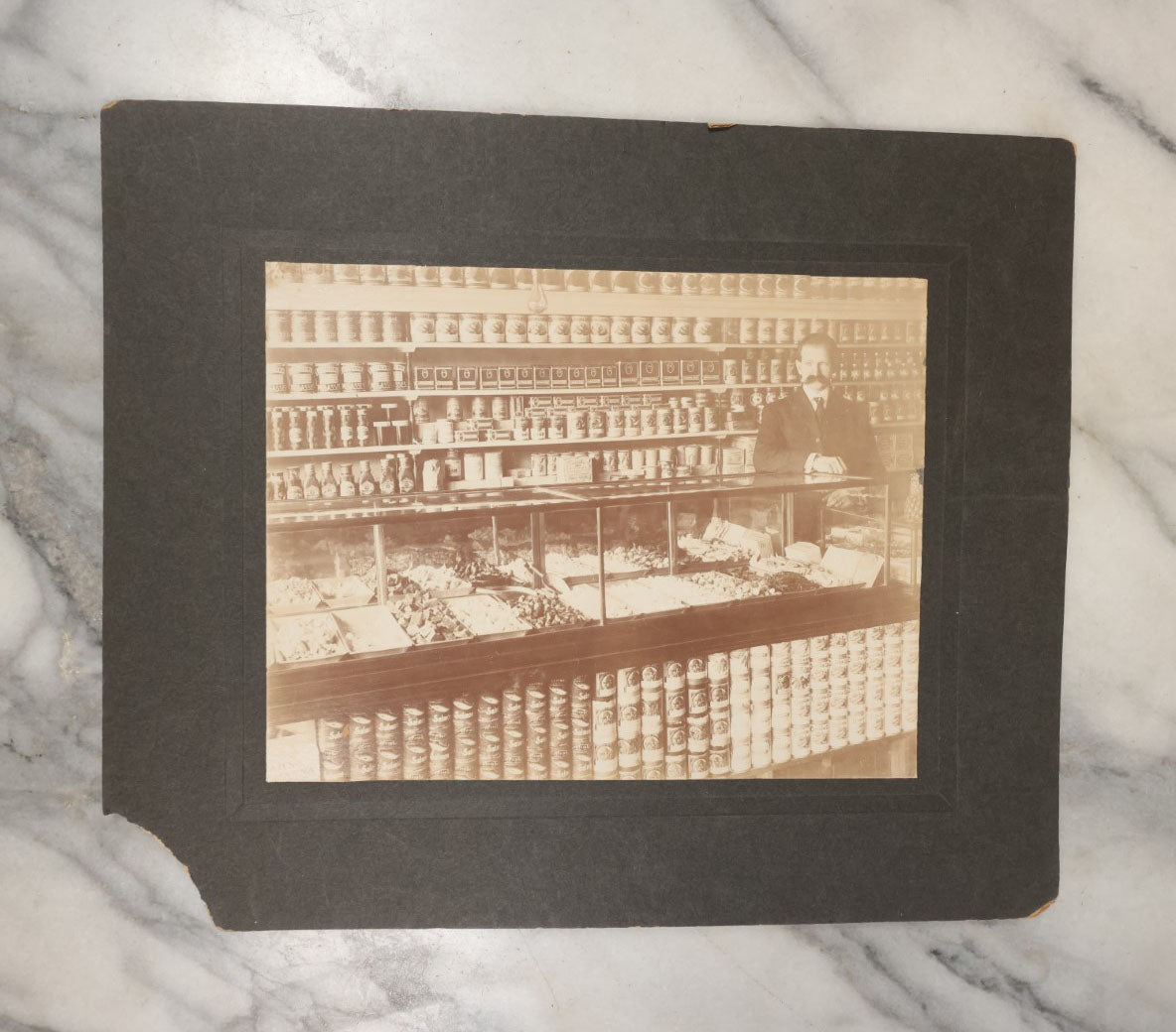 Lot 026 - Antique Boarded Occupational Photograph Of A Shopkeeper In A General Store, Identified As C.R. Johnson, 1907, Products Visible, Including Campbell's Soup Cans