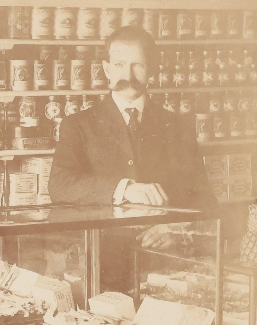 Lot 026 - Antique Boarded Occupational Photograph Of A Shopkeeper In A General Store, Identified As C.R. Johnson, 1907, Products Visible, Including Campbell's Soup Cans