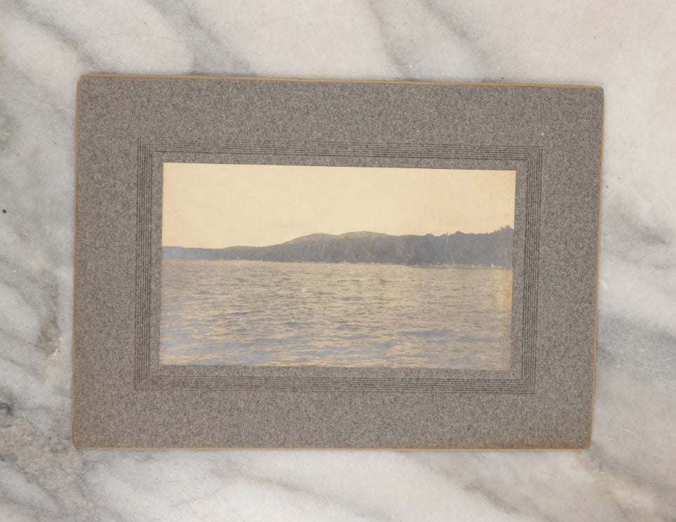 Lot 038 - Grouping Of Six Antique Boarded Photographs Related To Hunting And The Outdoors, Including Strung Up Deer, Group Photo With Man Shooting Rifle, Photo With People Holding Oars, Lake