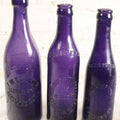 Lot 196 - Grouping Of Three Vintage And Antique Purple Glass Bottles, Including F.W. Kuenhold, Hartford, Connecticut, Sampson Springs Co., South Boston, And Brockton Bottling Co, Massachusetts