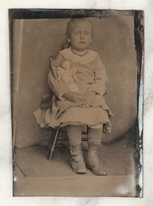 Lot 019 - Single Antique Tintype Photograph Of A Little Girl Seated In A Small Wooden Chair With Her Doll Tucker Under Her Arm