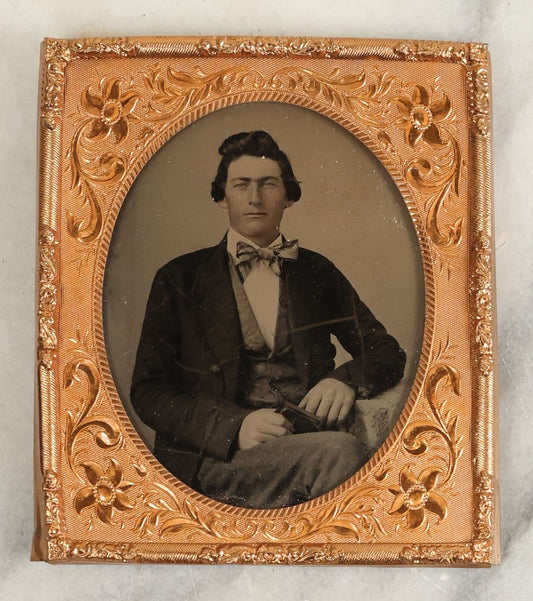 Lot 107 - Antique 1/6th Plate Ambrotype Of A Steely Eyed Young Man In A Suit And Bowtie Holding A Thermoplastic Photo Case In Lap, Note Crazing To Ambrotype Black Paint Backing, No Case