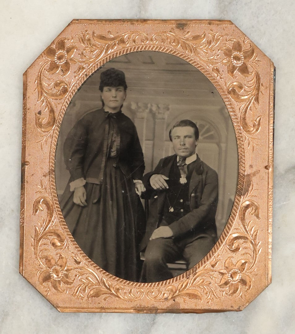 Lot 116 - Antique Matted Tintype Photograph Of A Younger Couple, Woman In Long Dress With Over Shirt, Man In Suit, With Tinted Cheeks, Man Seated