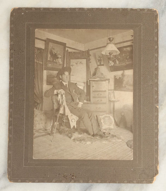 Lot 120 - Antique Boarded Photo Of A Young Man College Student, Likely In A Dorm Room, With Interior Scene Including Artwork, Early Light Fixture, Dresser, Pennant, Fur Rug, And More