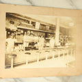 Lot 081 - Antique Boarded Photograph Of A Classic American Diner, With Workers Behind The Counter, Lots Of Signage, Stools