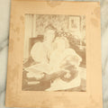 Lot 089 - Antique Boarded Photograph Of A Young Woman And Her Daughter Seated By A Piano Holding A Blurry, Moving Cat