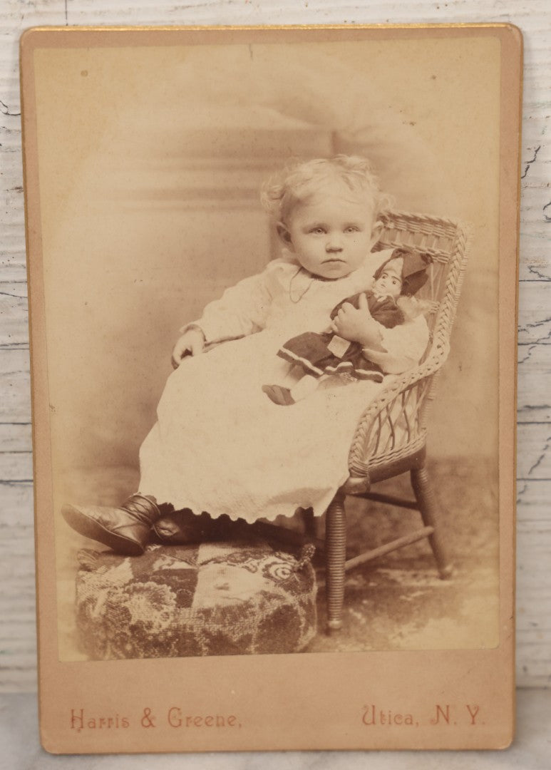 Lot 067 - Antique Cabinet Card Photograph Of A Young Baby Toddler Holding Her Doll, Seated In Chair, Harris & Greene Photographers, Utica, New York