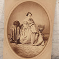 Lot 069 - Antique Matted Occupational Photograph Of An Adult Woman Seamstress, Pictured With Sewing Stand, And Scraggly Little Black Dog On Table To The Left, C.L. Obst Photographer, Pittsfield, Illinois