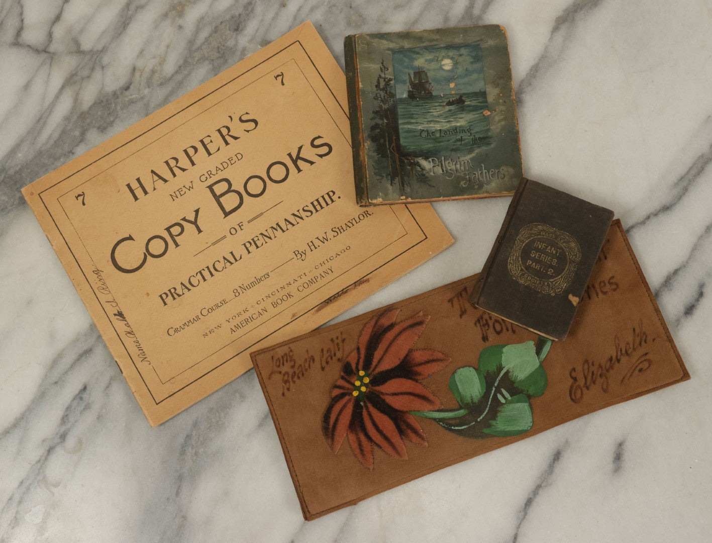 Lot 129 - Grouping Of Four Pieces Of Ephemera Including The Land Of The Pilgrim Fathers Book, Harper's Penmanship Book, Leather Blotter From Long Beach, California, And Infant Series Book