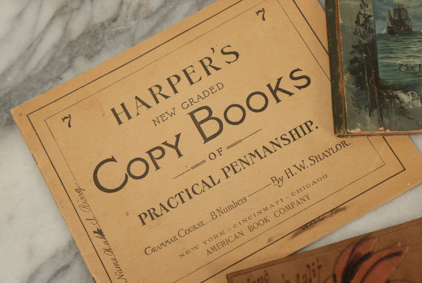 Lot 129 - Grouping Of Four Pieces Of Ephemera Including The Land Of The Pilgrim Fathers Book, Harper's Penmanship Book, Leather Blotter From Long Beach, California, And Infant Series Book