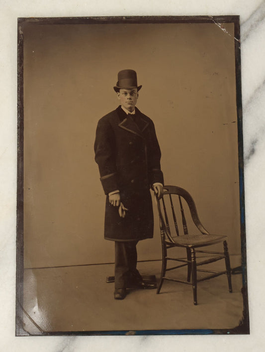 Lot 110 - Approximately Half Plate Antique Tintype Photograph Of A Young Man Holding A Glove Wearing A Tall Bowler Hat, With Posing Stand In Frame, Chair