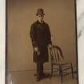 Lot 110 - Approximately Half Plate Antique Tintype Photograph Of A Young Man Holding A Glove Wearing A Tall Bowler Hat, With Posing Stand In Frame, Chair