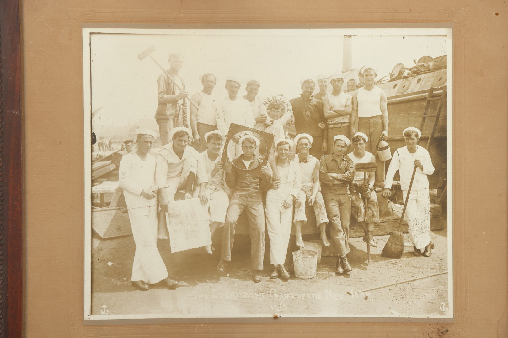 Lot 019 - Antique Boarded Photograph In Frame Of "The Steamboat Gang Of The New York," 1915, Occupational Photos Of Navy Sailors On Dock, With Tools Of The Trade, Other Workers In Background, U.S.S. New York (BB-34), 15-1/2" x 13-1/2"