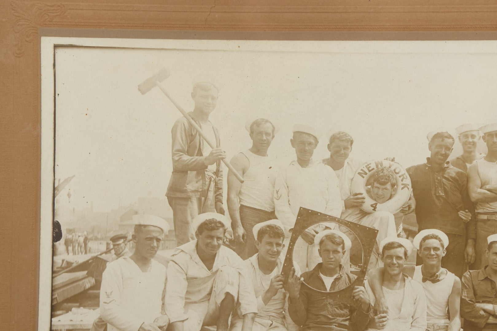 Lot 019 - Antique Boarded Photograph In Frame Of "The Steamboat Gang Of The New York," 1915, Occupational Photos Of Navy Sailors On Dock, With Tools Of The Trade, Other Workers In Background, U.S.S. New York (BB-34), 15-1/2" x 13-1/2"