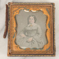 Lot 026 - Antique 1/6th Plate Daguerreotype Photograph Of A Middle Aged Woman With Hand Tinted Coloring, Blueish Dress, Gold Jewelry, Pink Tinting To Face, In Half Leatherette Union Case With Ship, Castle Scene On Verso