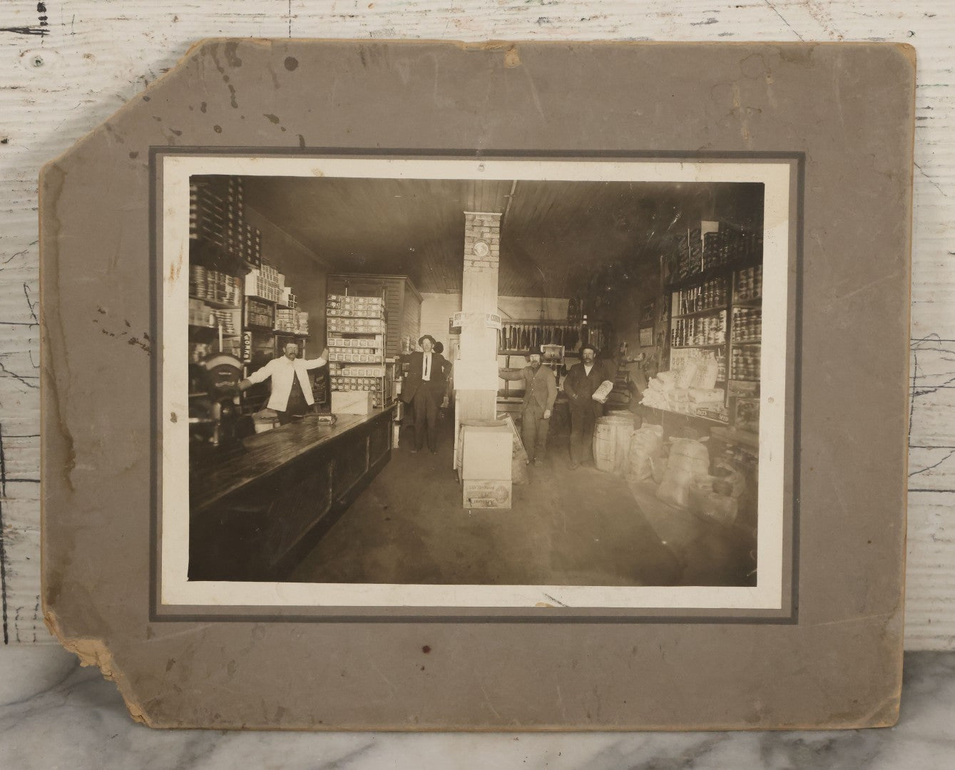 Lot 080 - Antique Boarded Occupational Photograph Of The Interior Of A General Store With Four Men In Frame, Many Products, Advertisements, Note Corner Losses