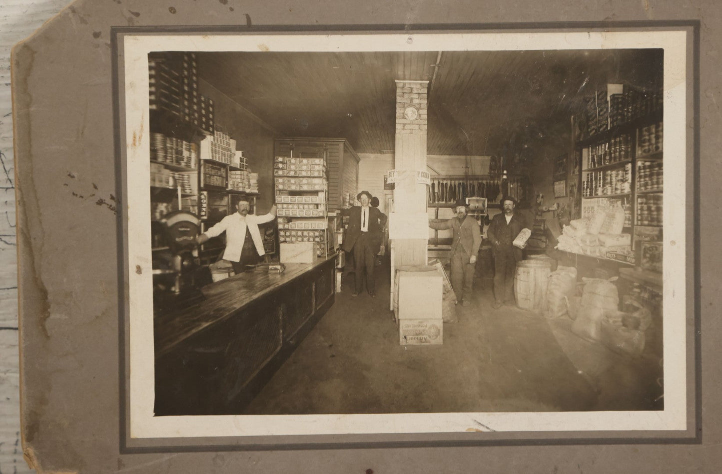 Lot 080 - Antique Boarded Occupational Photograph Of The Interior Of A General Store With Four Men In Frame, Many Products, Advertisements, Note Corner Losses