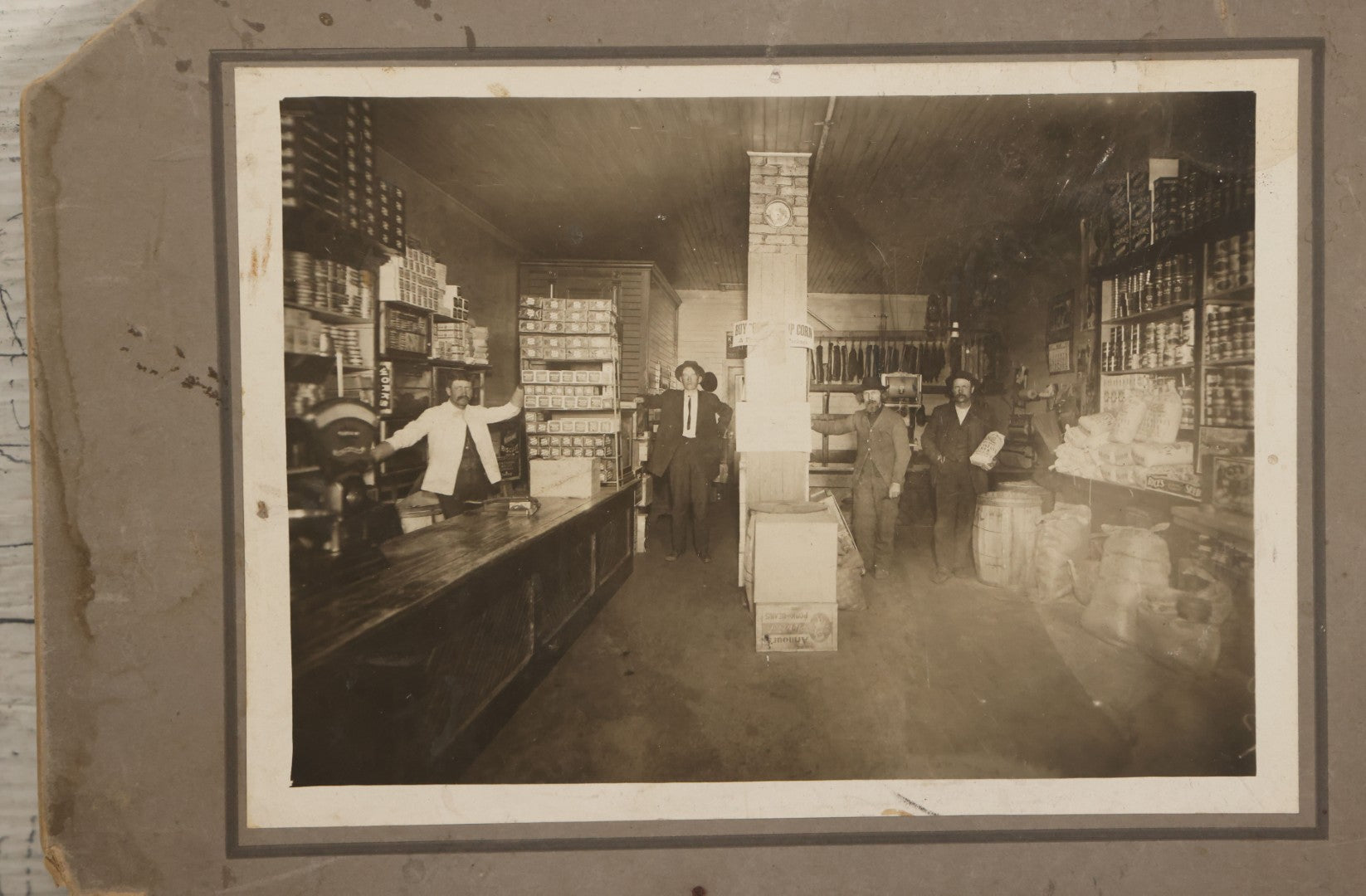Lot 080 - Antique Boarded Occupational Photograph Of The Interior Of A General Store With Four Men In Frame, Many Products, Advertisements, Note Corner Losses