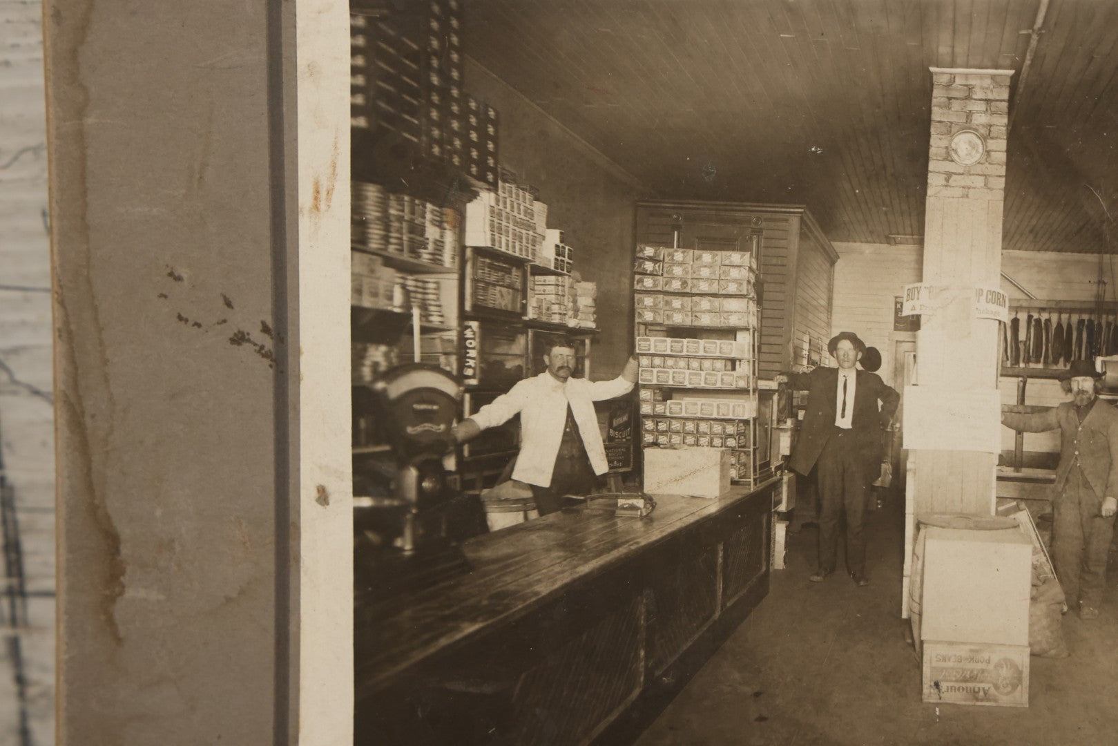 Lot 080 - Antique Boarded Occupational Photograph Of The Interior Of A General Store With Four Men In Frame, Many Products, Advertisements, Note Corner Losses