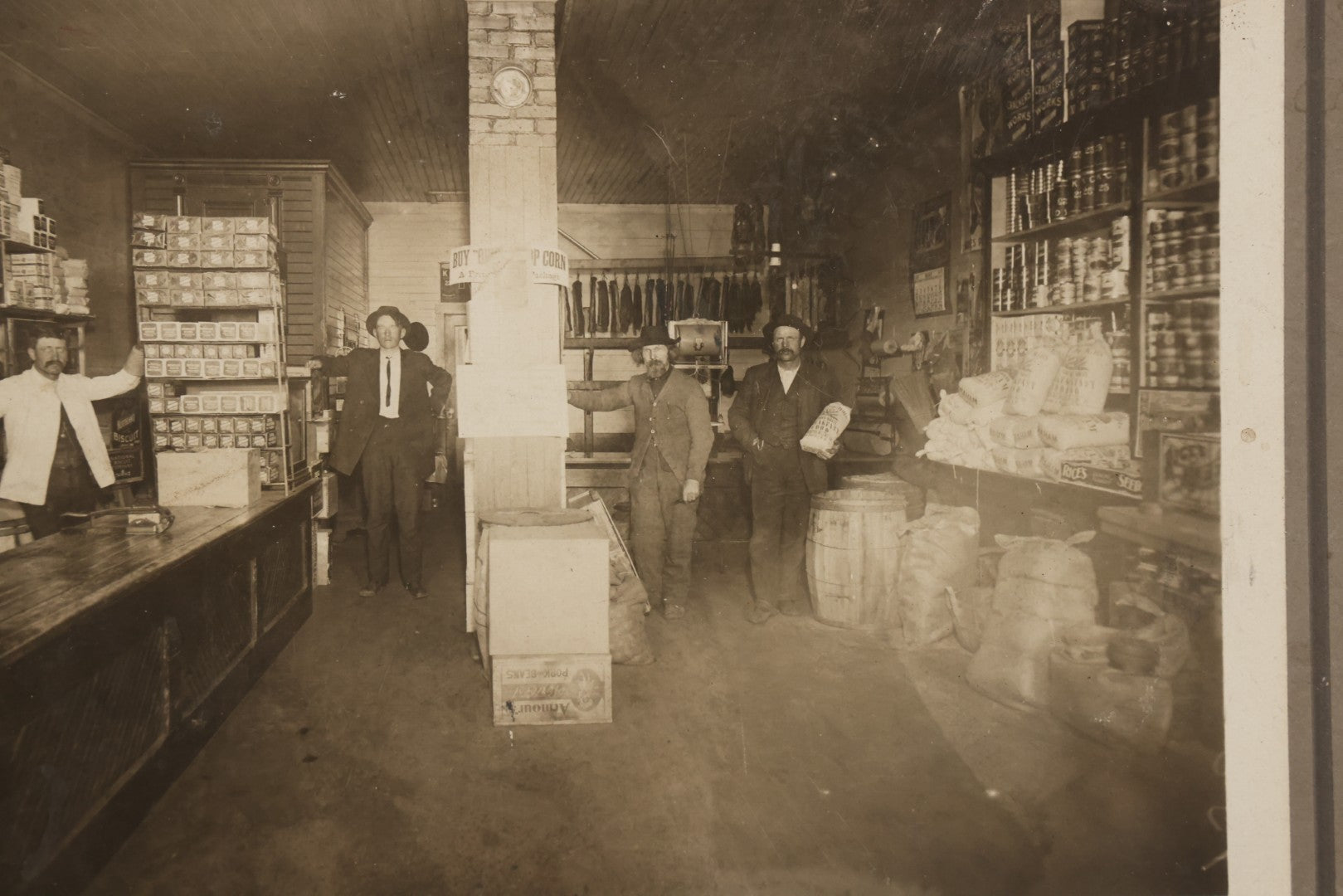 Lot 080 - Antique Boarded Occupational Photograph Of The Interior Of A General Store With Four Men In Frame, Many Products, Advertisements, Note Corner Losses