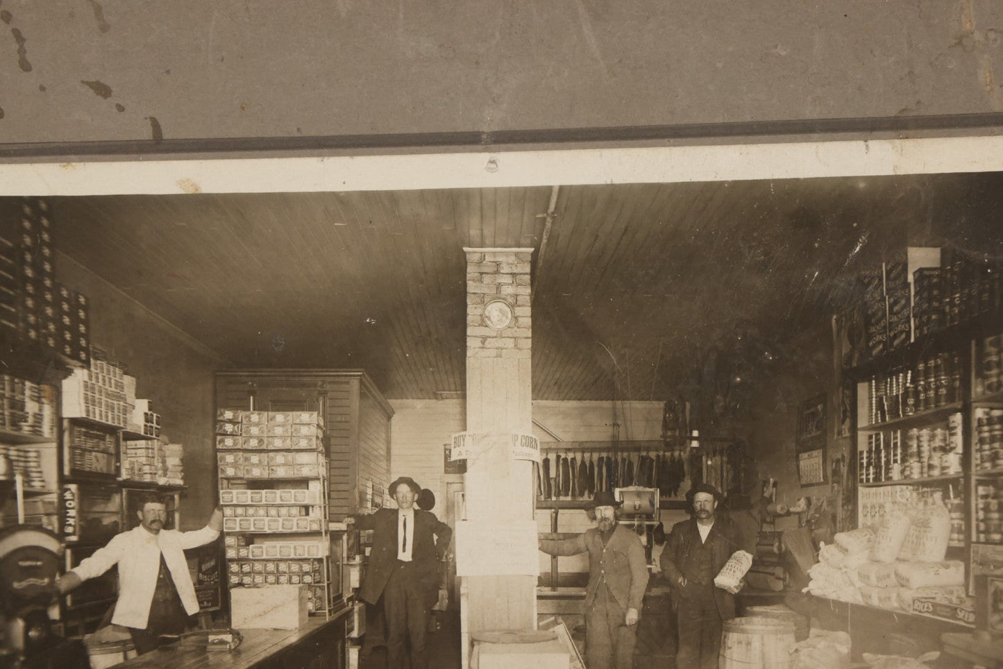 Lot 080 - Antique Boarded Occupational Photograph Of The Interior Of A General Store With Four Men In Frame, Many Products, Advertisements, Note Corner Losses