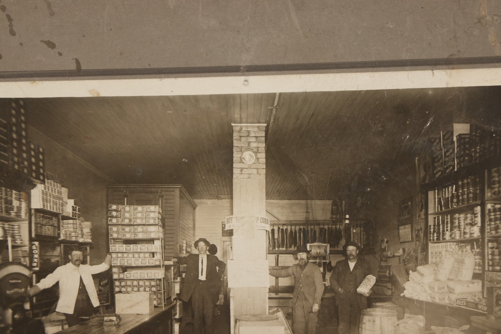 Lot 080 - Antique Boarded Occupational Photograph Of The Interior Of A General Store With Four Men In Frame, Many Products, Advertisements, Note Corner Losses