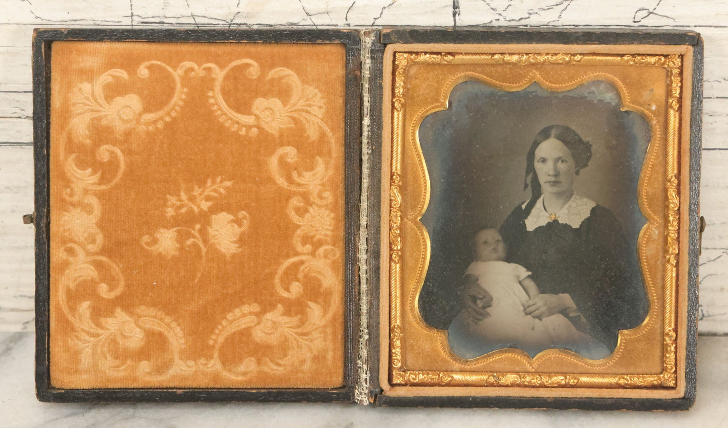 Lot 027 - Antique 1/6th Plate Ambrotype Photograph Of Young Mother Holding Newborn Baby, Wearing Tinted Jewelry, In Full Leatherette Union Case, Note Spine Repaired With Tape