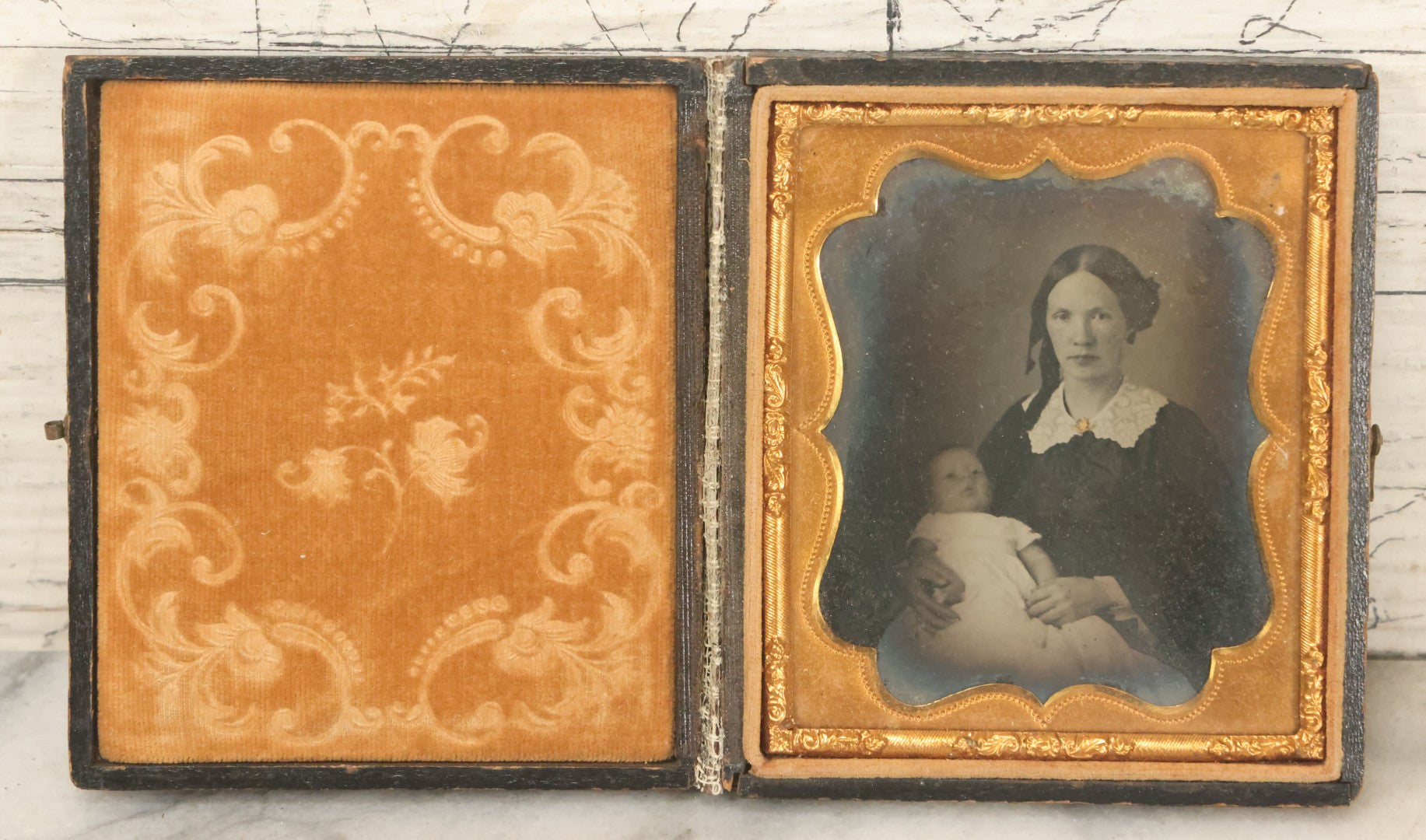 Lot 027 - Antique 1/6th Plate Ambrotype Photograph Of Young Mother Holding Newborn Baby, Wearing Tinted Jewelry, In Full Leatherette Union Case, Note Spine Repaired With Tape