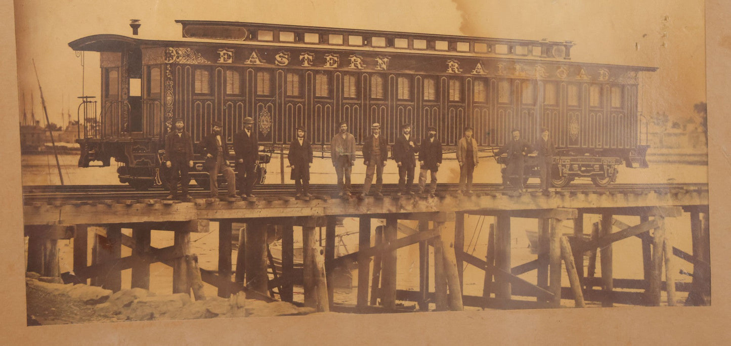 Lot 037 - Antique Boarded Occupational Photograph Of Newly Built Eastern Railroad Passenger Train Car, With Workers Pictured On Train Track, In Front Of Harbor, In Frame, Note Water Stains, 15-5/8" x 11-1/4"