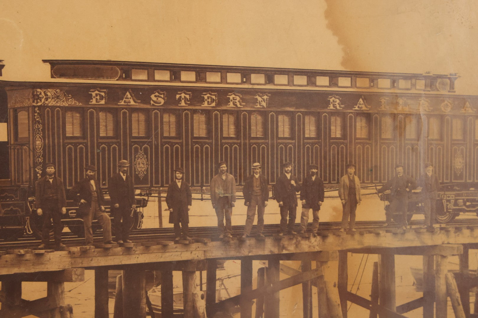 Lot 037 - Antique Boarded Occupational Photograph Of Newly Built Eastern Railroad Passenger Train Car, With Workers Pictured On Train Track, In Front Of Harbor, In Frame, Note Water Stains, 15-5/8" x 11-1/4"