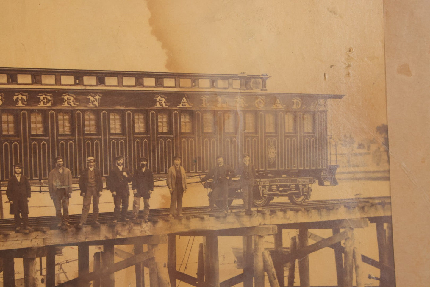 Lot 037 - Antique Boarded Occupational Photograph Of Newly Built Eastern Railroad Passenger Train Car, With Workers Pictured On Train Track, In Front Of Harbor, In Frame, Note Water Stains, 15-5/8" x 11-1/4"