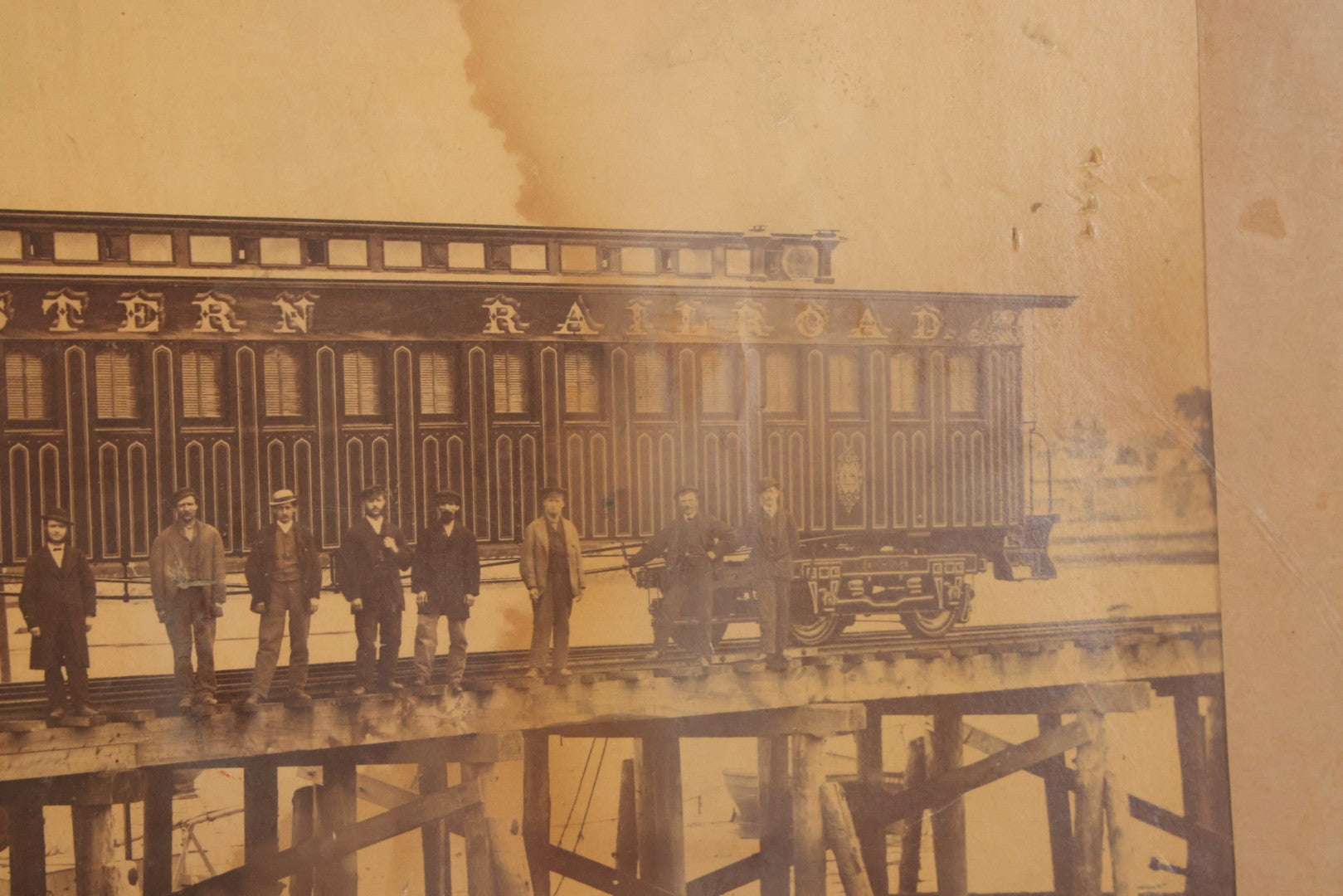 Lot 037 - Antique Boarded Occupational Photograph Of Newly Built Eastern Railroad Passenger Train Car, With Workers Pictured On Train Track, In Front Of Harbor, In Frame, Note Water Stains, 15-5/8" x 11-1/4"